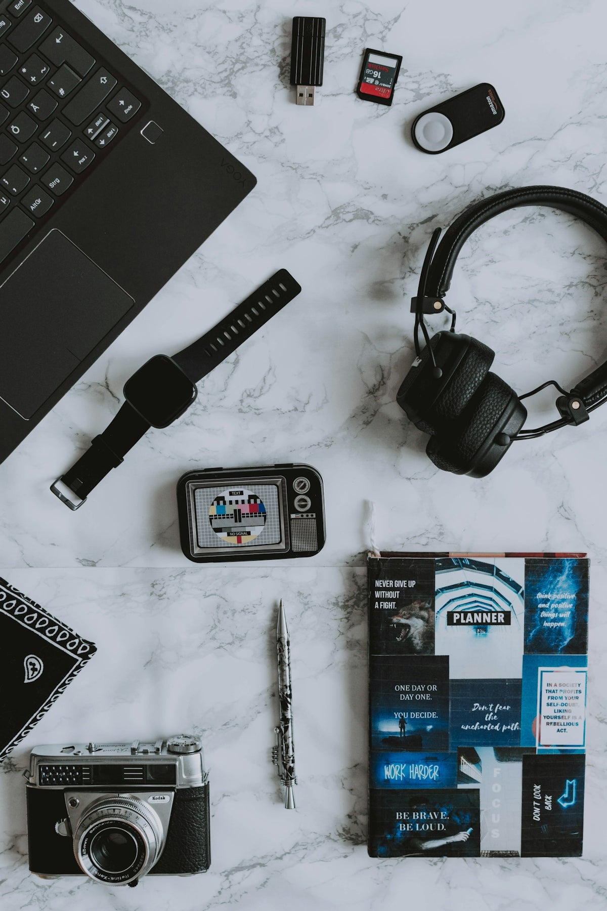 black wireless headphones near black USB flash drive, black laptop computer, black digital camera, black and silver bridge camera, and hardbound book